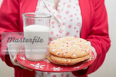 Woman holding Christmas cookies and glass of milk on plate