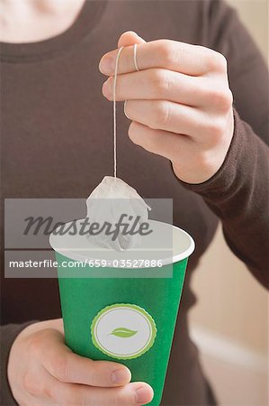 Woman holding a tea bag over a paper cup