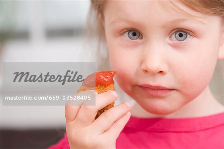 Little girl holding chicken nugget with ketchup