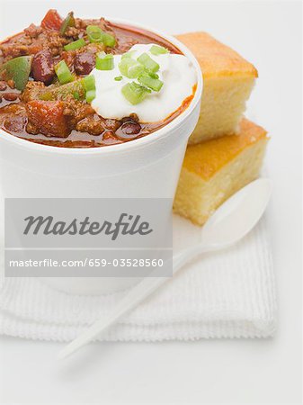 Chili con carne with sour cream in polystyrene cup, cornbread