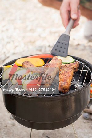 Hand turning vegetables on barbecue with barbecue tongs