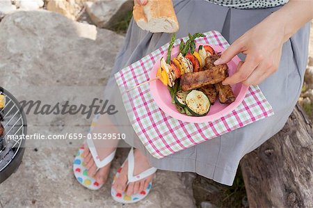 Woman eating grilled food and baguette on river bank