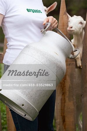 Woman with milk can in front of goat stall