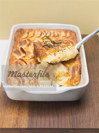 Potato gratin in baking dish with piece on server