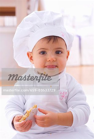 Little girl in chef's hat eating biscuit