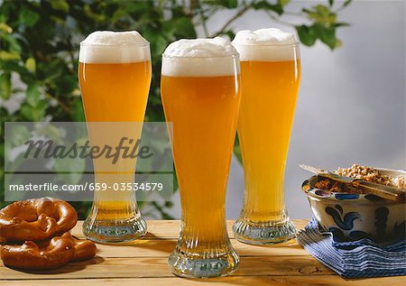 Three glasses of wheat beer on wooden table with pretzels & lard