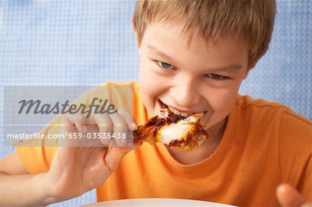 Young boy biting into a chicken drunstick