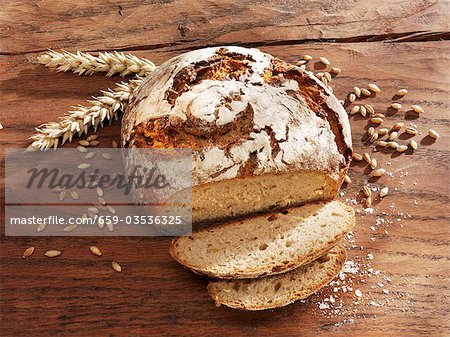 Rustic loaf of bread, partly sliced, ears & grains of wheat