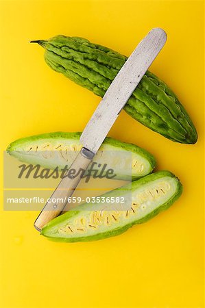 Whole and Halved Bitter Melon with Knife on Yellow Background