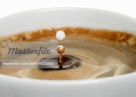 A drop of milk falling into a cup of coffee (close-up)