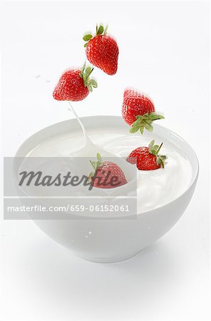 Strawberries falling into a bowl of yogurt