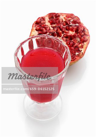 A glass of pomegranate juice with half a pomegranate in the background