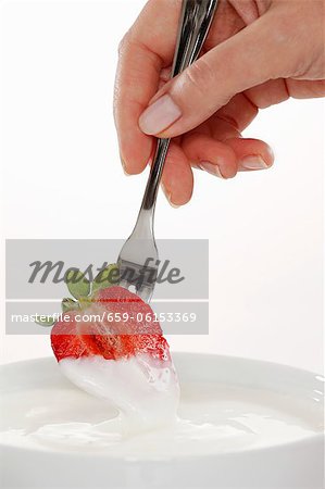 Half a strawberry being hand dipped in organic yogurt