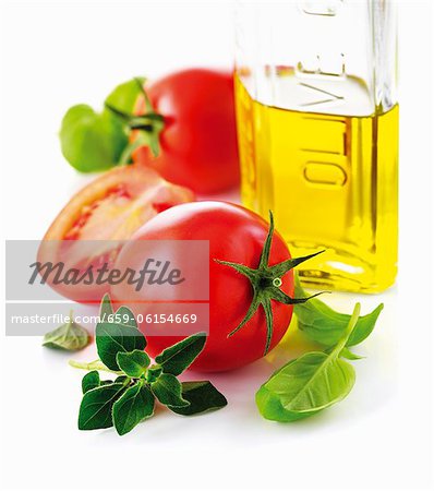 Tomatoes, a bottle of olive oil and fresh herbs (close-up)