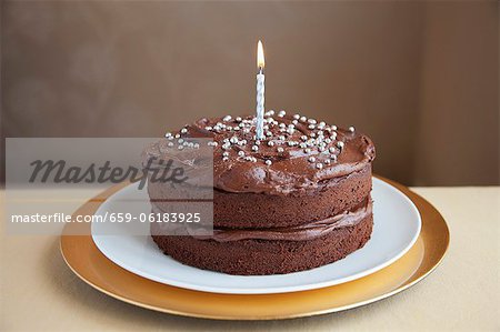 A chocolate cake decorated with silver balls and a candle