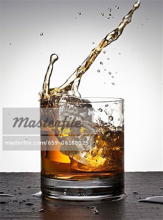 Premium Photo  Glass with whiskey and falling ice cube with splashes