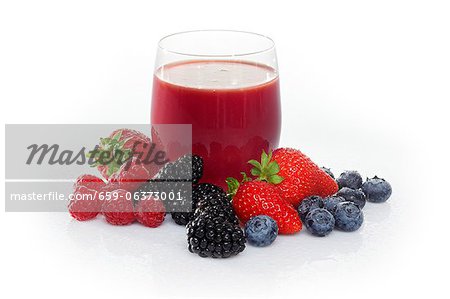 A glass of fruits of the forest juice surrounded by fruits of the forest