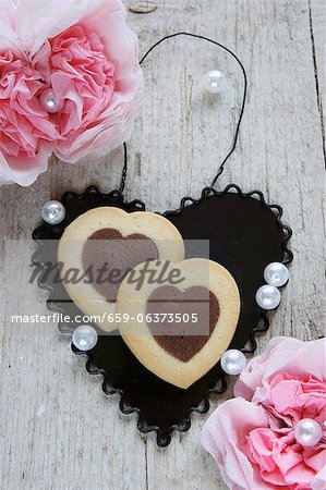 Bi-coloured heart-shaped biscuits on a black metal heart between paper carnations