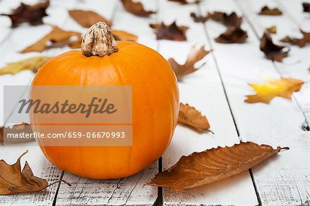 A pumpkin and autumnal leave on a wooden table A pumpkin and autumnal leave on a wooden table