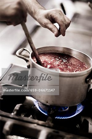 A cook seasoning tomato sauce with salt