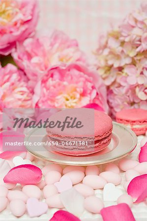 A pink macaroon on a silver plate, surrounded by sugared almonds, peonies and rose petals