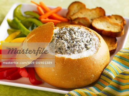 Spinach Dip in a Bread Bowl with Sliced Veggies and Toasted Bread Slices for Dipping