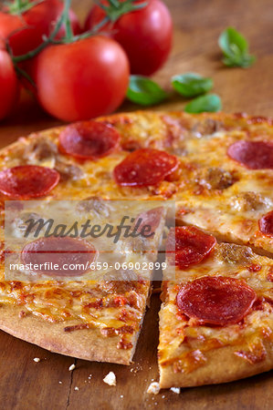 Pepperoni and Sausage Pizza with a Slice Partially Removed; Fresh Tomatoes and Basil in the Background Pepperoni and Sausage Pizza with a Slice Partially Removed; Fresh Tomatoes and Basil in the Background
