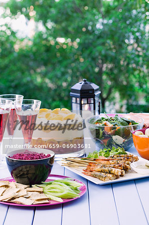 A table in the garden, laid with prawn skewers, beetroot dip, spinach salad and a trifle