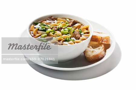 A Bowl of Bourbon Beef and Noodle Soup with Two Slices of Bread; White Background