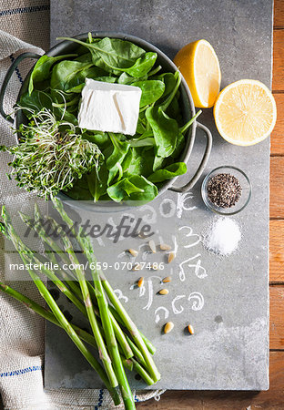 A still life of spinach, asparagus, cress, feta, pine nuts, lemons, salt and pepper