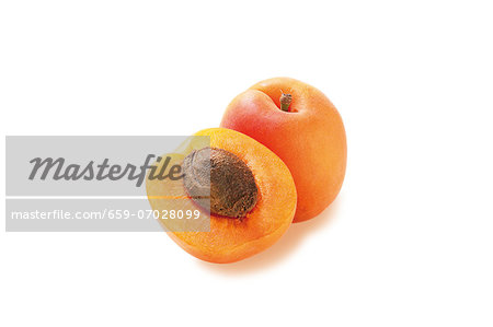 A whole and a half apricot against a white background