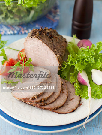 Partially Sliced Pork Roast on a Platter with Greens and Radishes