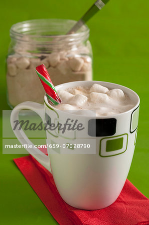 White hot chocolate with marshmallows in a mug, with dry ingredients for making it in the background