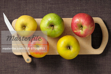 Assorted apples on a chopping board with a knife