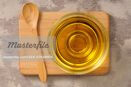 Olive oil in a glass dish on a chopping board with a wooden spoon Olive oil in a glass dish on a chopping board with a wooden spoon