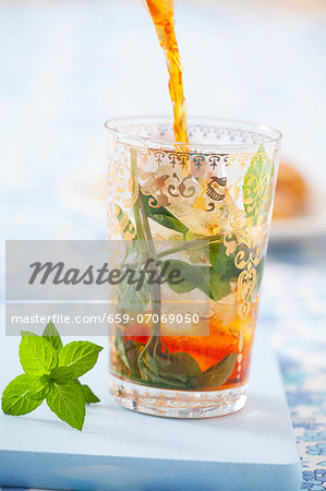 Iced tea being poured into a glass with ice cubes and mint