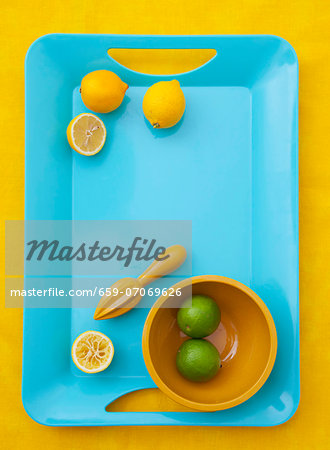 Lemons, whole and halved, with a lemon squeezer; limes in a bowl Lemons, whole and halved, with a lemon squeezer; limes in a bowl