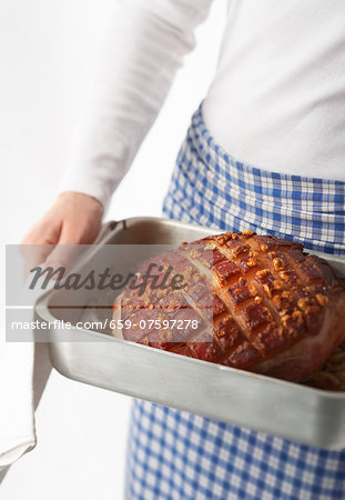 A woman holding a roasting tin with a roast crackling joint of pork