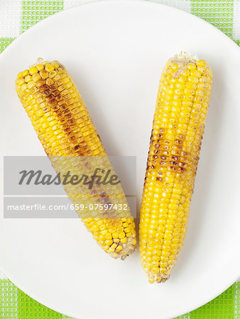 Two barbecued corn cobs on a plate (view from above)