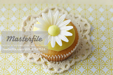 A cupcake decorated with an oxeye daisy on a lace doily