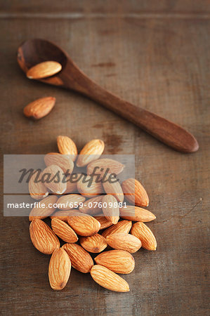 Almonds on a wooden surface with a wooden spoon