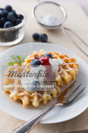 Waffles with icing sugar, blueberries, cream and fruit sauce