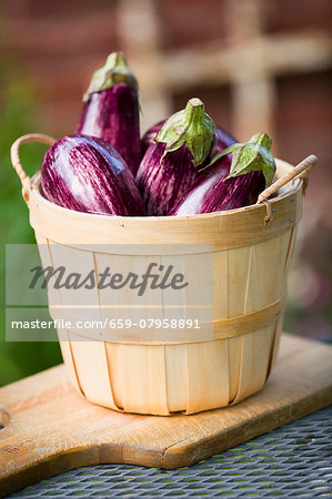 Aubergines in a wooden basket on a chopping board
