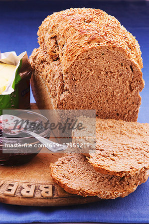 A loaf of bread with brewers grains, two slices cut off, next to butter and jam