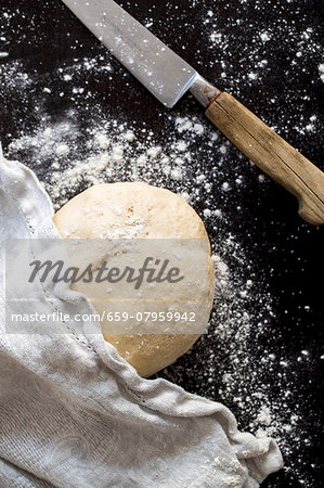 A ball of pizza dough with flour, a cloth and a knife