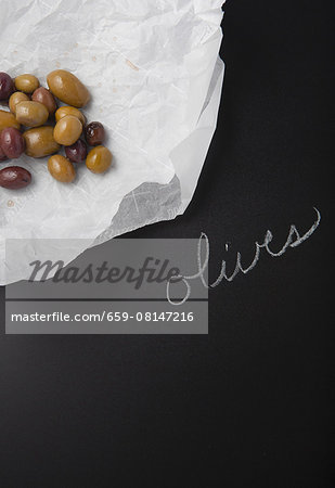 Olives on a piece of paper on a slate surface with a label