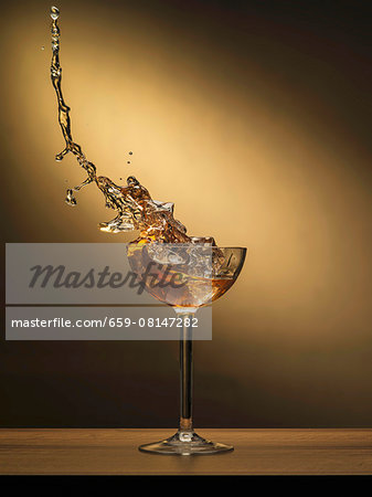 A cocktail splashing out of a glass with ice cubes