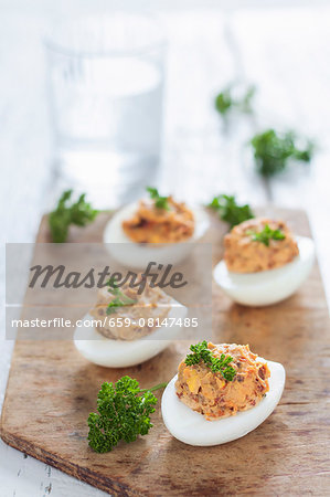 Devilled eggs with dried tomatoes and fresh parsley on a wooden board