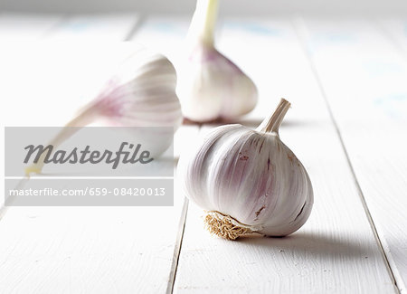 Three bulbs of garlic on a white wooden surface