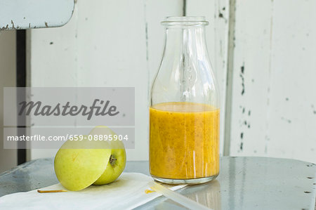 A mango and orange smoothie with chia seeds in a bottle on an old chair with an apple